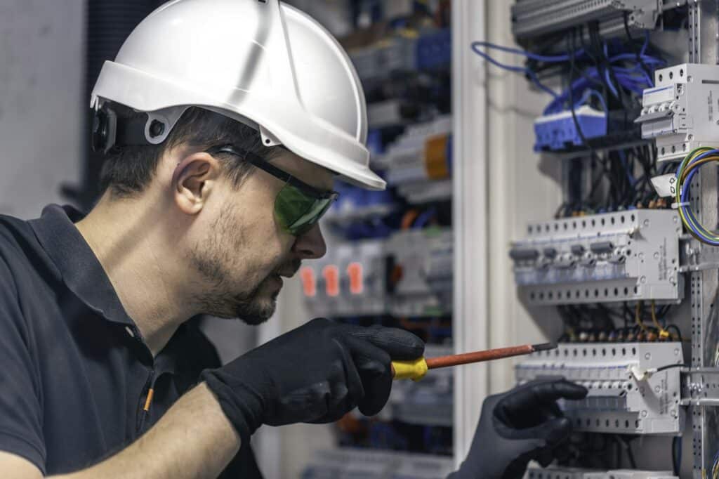 A male electrician works in a switchboard using an electrical connection cable.